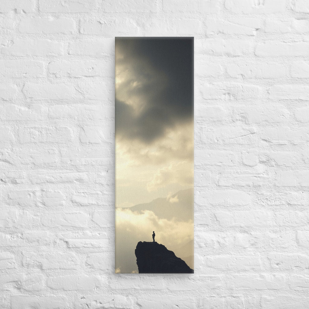 A Summit in Light, tall wrapped canvas print: a lone figure atop a dark rocky summit with radiant light breaking through clouds.