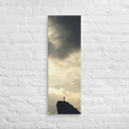 A Summit in Light, tall wrapped canvas print: a lone figure atop a dark rocky summit with radiant light breaking through clouds.