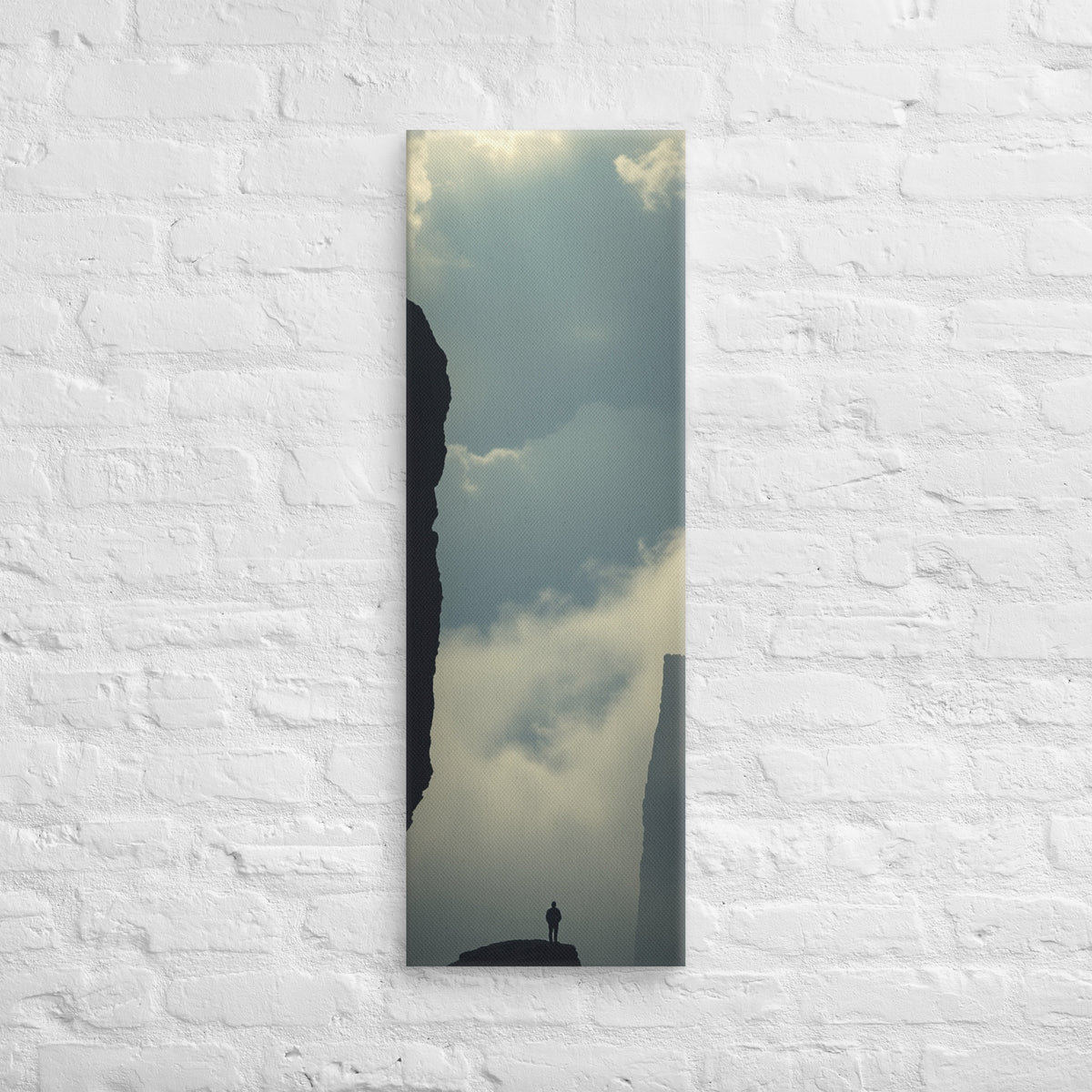 Between the Dark Walls, tall wrapped canvas print: a solitary figure on a rock fin between two sheer dark cliff walls, mist in the gorge.