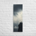 Where the Clouds Break, tall wrapped canvas print: a lone figure on a high cliff as dark clouds split open with light behind.