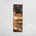 Two at the Tide, tall wrapped canvas print: two figures on wet sand under a fiery orange sunset over the sea.