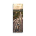 The Long Way Home, tall wrapped canvas print: a long empty road through green and gold farmland stretching to a luminous horizon under breaking sun-shafts.