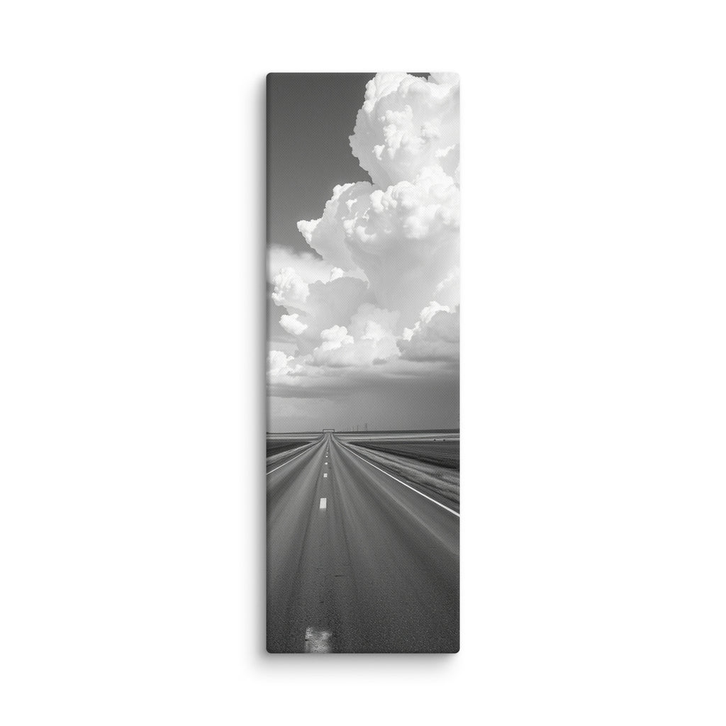 Distance In Silver, tall wrapped canvas print: a black-and-white view of a straight road through plains beneath an enormous towering cumulus cloud.