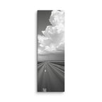 Distance In Silver, tall wrapped canvas print: a black-and-white view of a straight road through plains beneath an enormous towering cumulus cloud.