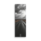 The Weight Of Weather, tall wrapped canvas print: a near-monochrome view of a road beneath an immense wall of dark storm clouds.
