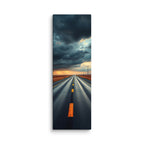 At The Edge Of The Storm, tall wrapped canvas print: a long straight road across russet plains under massive dark storm clouds with amber sunset light on the horizon.