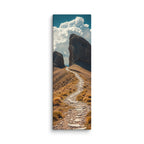 The Way Through Stone, tall wrapped canvas print: a stone-paved path passing between two massive rock towers under cumulus clouds.