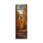 A Canopy Of October, tall wrapped canvas print: a dirt path through a tunnel of golden autumn trees toward distant mountains.