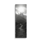 The Silent Ascent, tall wrapped canvas print: a black-and-white winding mountain path climbing toward sunlight breaking through clouds.