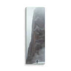 Winter Keeps Watch, tall wrapped canvas print: a lone figure standing on snow before a towering grey rock spire dissolving into fog.