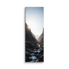 First Light In The Cleft, tall wrapped canvas print: the sun bursting over a dark rocky cleft as a stream flows toward the light.