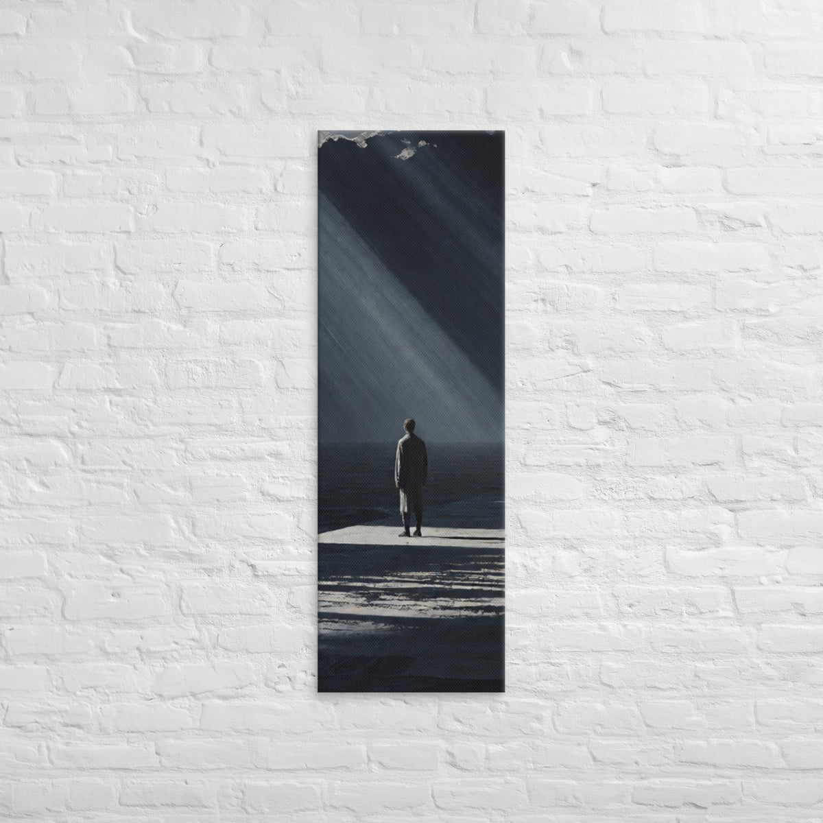In a Shaft of Light, tall wrapped canvas print: a lone figure at the water's edge beneath dramatic shafts of light breaking through dark clouds.