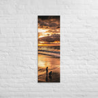At the Water's Edge, tall wrapped canvas print: two figures on wet sand at the water's edge under a blazing golden sunset.