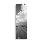 Distance In Silver, tall wrapped canvas print: a black-and-white view of a straight road through plains beneath an enormous towering cumulus cloud.