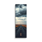 Before The Rain, tall wrapped canvas print: a straight road through amber fields under towering dark storm clouds, rain falling in the distance.