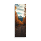 The Peak Beyond The Trees, tall wrapped canvas print: a dirt road through golden autumn trees toward a distant rocky peak.