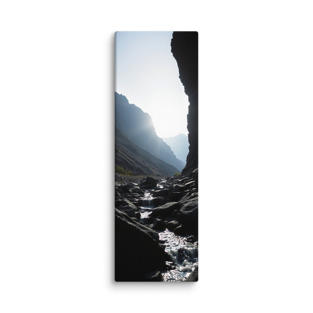 A Thread Through Shadow, tall wrapped canvas print: a bright stream winding through dark shadowed rocks toward hazy mountain ridges.