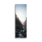 First Light In The Cleft, tall wrapped canvas print: the sun bursting over a dark rocky cleft as a stream flows toward the light.