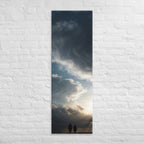 Beneath the Silver Sky, tall wrapped canvas print: two silhouetted figures beneath a vast swirling silver-grey cloudy sky with light breaking through.
