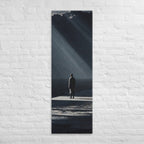In a Shaft of Light, tall wrapped canvas print: a lone figure at the water's edge beneath dramatic shafts of light breaking through dark clouds.