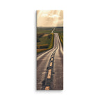 The Long Way Home, tall wrapped canvas print: a long empty road through green and gold farmland stretching to a luminous horizon under breaking sun-shafts.