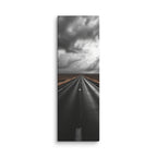 The Weight Of Weather, tall wrapped canvas print: a near-monochrome view of a road beneath an immense wall of dark storm clouds.