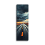 At The Edge Of The Storm, tall wrapped canvas print: a long straight road across russet plains under massive dark storm clouds with amber sunset light on the horizon.