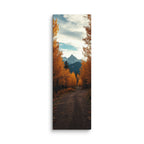The Peak Beyond The Trees, tall wrapped canvas print: a dirt road through golden autumn trees toward a distant rocky peak.