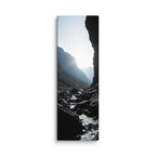 A Thread Through Shadow, tall wrapped canvas print: a bright stream winding through dark shadowed rocks toward hazy mountain ridges.