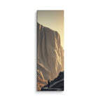 The Glowing Wall, tall wrapped canvas print: a lone figure on a dark ridge before a vast cliff wall glowing amber at sunset.