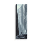 A Pale Immensity, tall wrapped canvas print: a lone figure on dark rocks before a vast pale ice cliff with shafts of light.