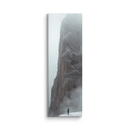 Winter Keeps Watch, tall wrapped canvas print: a lone figure standing on snow before a towering grey rock spire dissolving into fog.