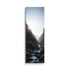 First Light In The Cleft, tall wrapped canvas print: the sun bursting over a dark rocky cleft as a stream flows toward the light.